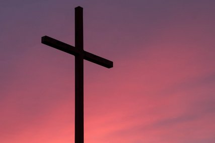 Ein schwarzes Kreuz vor einem rot erleuchteten Himmel. - Copyright: Aaron Burden / Unsplash
