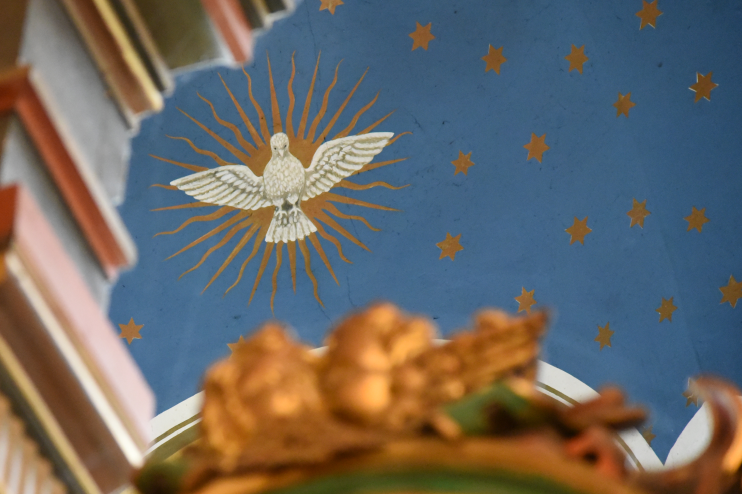 Ein weißer Vogel fliegt vor einer strahlenden Sonne, auf das Kirchengewölbe gemalt.