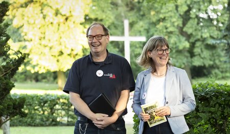 Ein Mann und eine Frau stehen lachend auf einem Friedhof. 