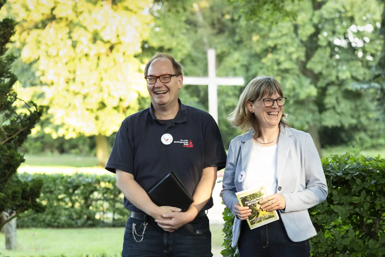 Ein Mann und eine Frau stehen lachend auf einem Friedhof. 