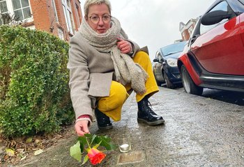 Eine Frau legt eine Rose auf einem goldenen Gedenkstein auf einer Straße nieder.  - Copyright: Bastian Modrow