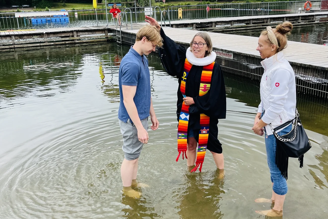 Pastorin Nicola Nehmzow tauft Ben Joel Hinz. Mit dabei: Mutter Kati Hinz. Sie stehen alle im Wasser, die Pastorin hält eine Hand über den Kopf des jungen Mannes.