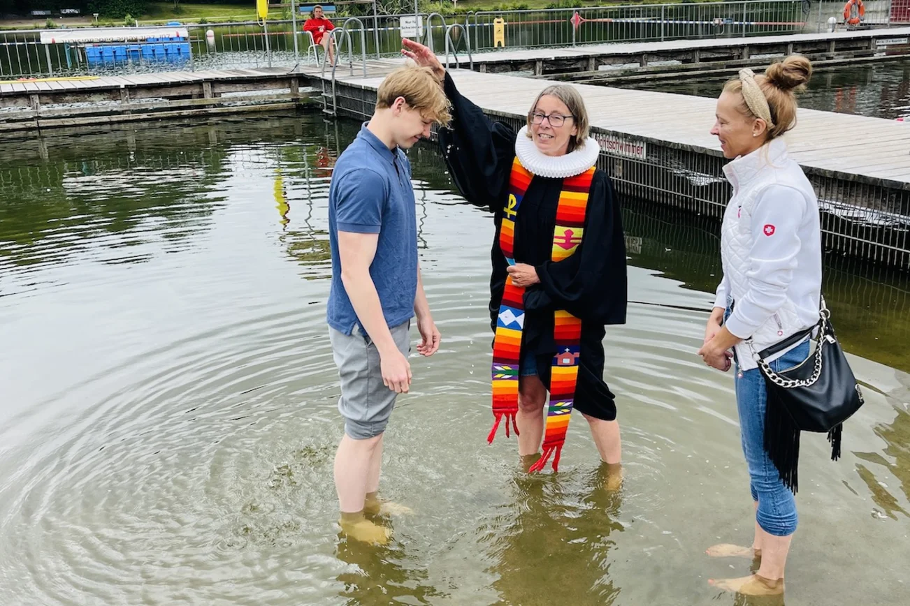 Pastorin Nicola Nehmzow tauft Ben Joel Hinz. Mit dabei: Mutter Kati Hinz. Sie stehen alle im Wasser, die Pastorin hält eine Hand über den Kopf des jungen Mannes.