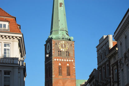 Der Turm von der St.-Jakobi-Kirche ragt in den blauen Himnmel, links und rechts die Fassaden Lübecker Häuser - Copyright: Ev.-Luth. Kirchenkreis Lübeck-Lauenburg