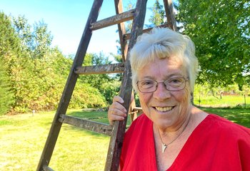 Eine Frau steht lächelnd an einer Leiter in ihrem Garten.  - Copyright: Bastian Modrow