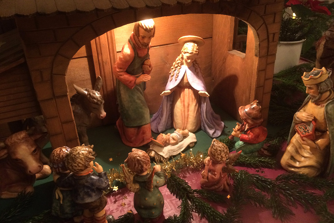 Eine Holzkrippe mit Maria, Josef, dem Jesukind, einem knienenden König, 2 kleine Engelfiguren, kleine knabenhafte Hirten, sowie Esel und Kuh sind auf dem Bild zu sehen.