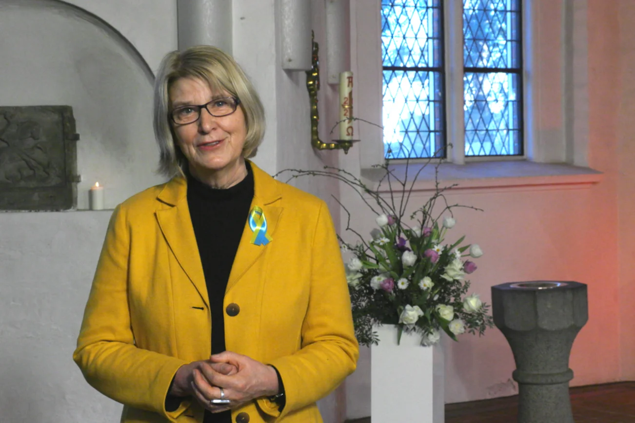 Eine Frau steht in einer Kirche und lächelt in die Kamera. 