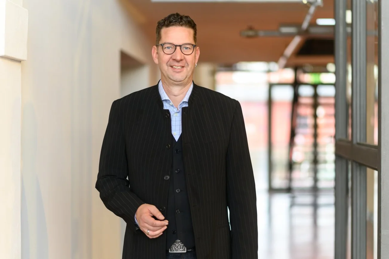 Ein Mann steht in einem Flur und lächelt in die Kamera. 