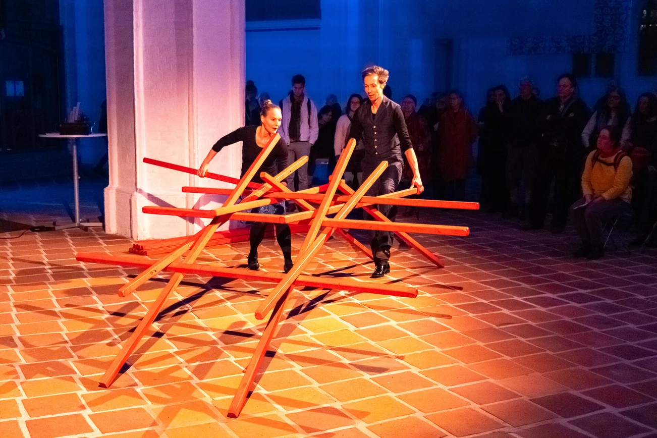 Eine Frau und ein Mann halten eine Art übergroßes Mikadospiel in einem Kirchraum.