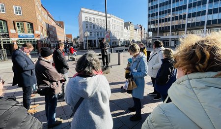 Auf dem Klingenberg, ein freier Platz vor mehreren Gebäuden in der Innenstadt von Lübeck steht eine Gruppe bei Sonnenschein und blauen Himmel