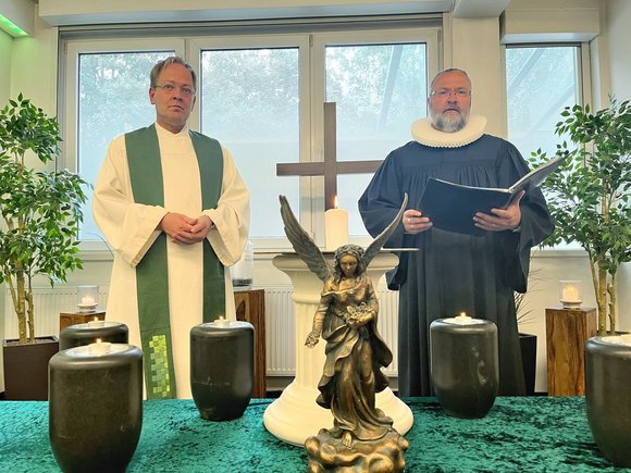 Zwei Pastoren in einem Raum vor einem Tisch mit Urnen