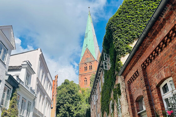 Im Hintergrund ragt der Turm von St. Aegidien in den blauen Himmel, welcher mit weißen Schleierwolken verhangen ist. Im Vordergrund die Häuserfronten der Weberstraße - Copyright: Steffi Niemann