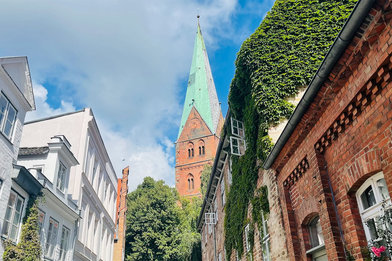 Im Hintergrund ragt der Turm von St. Aegidien in den blauen Himmel, welcher mit weißen Schleierwolken verhangen ist. Im Vordergrund die Häuserfronten der Weberstraße - Copyright: Steffi Niemann