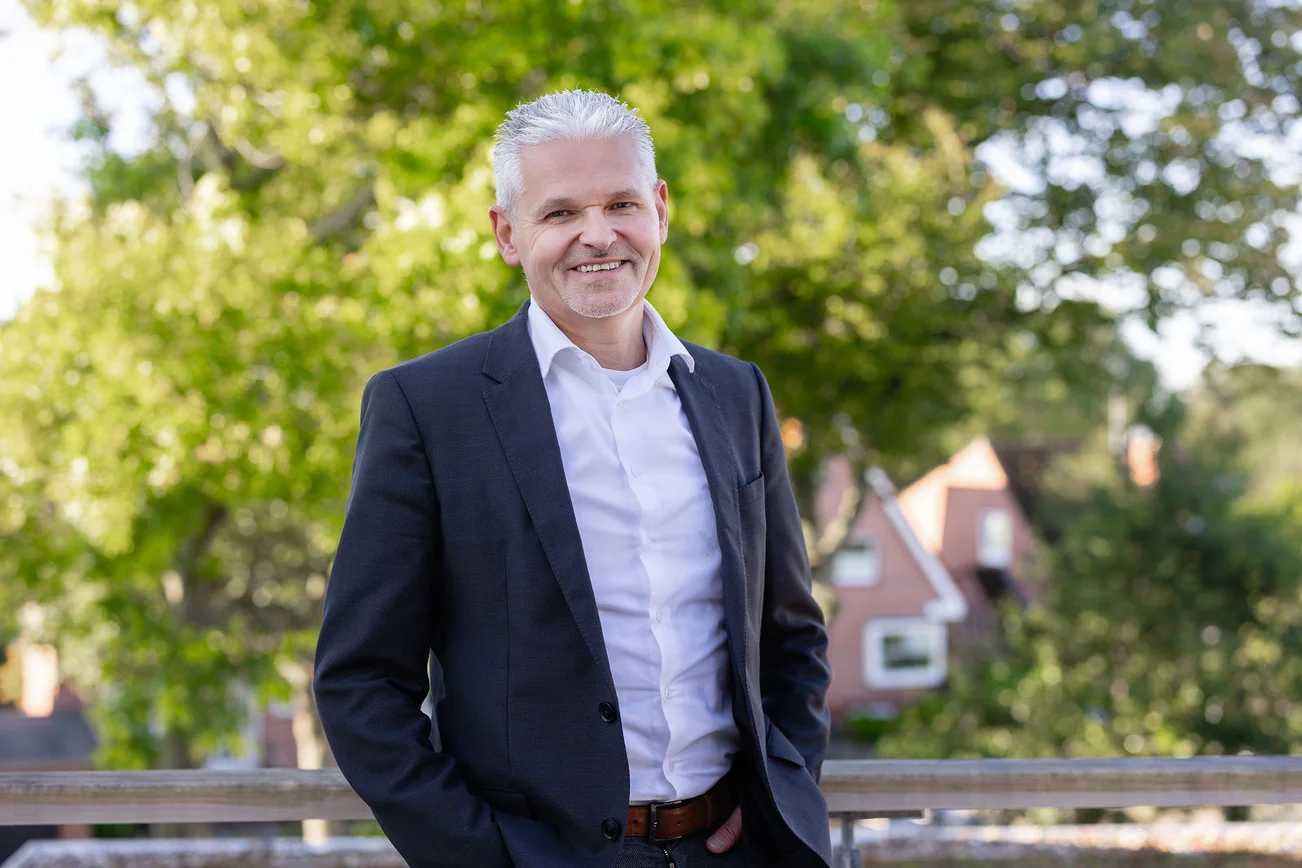 Ein Mann mit kurzen grauen Haaren lächelt in die Kamera. Er trägt ein helles Hemd und ein dunkles Sakko.