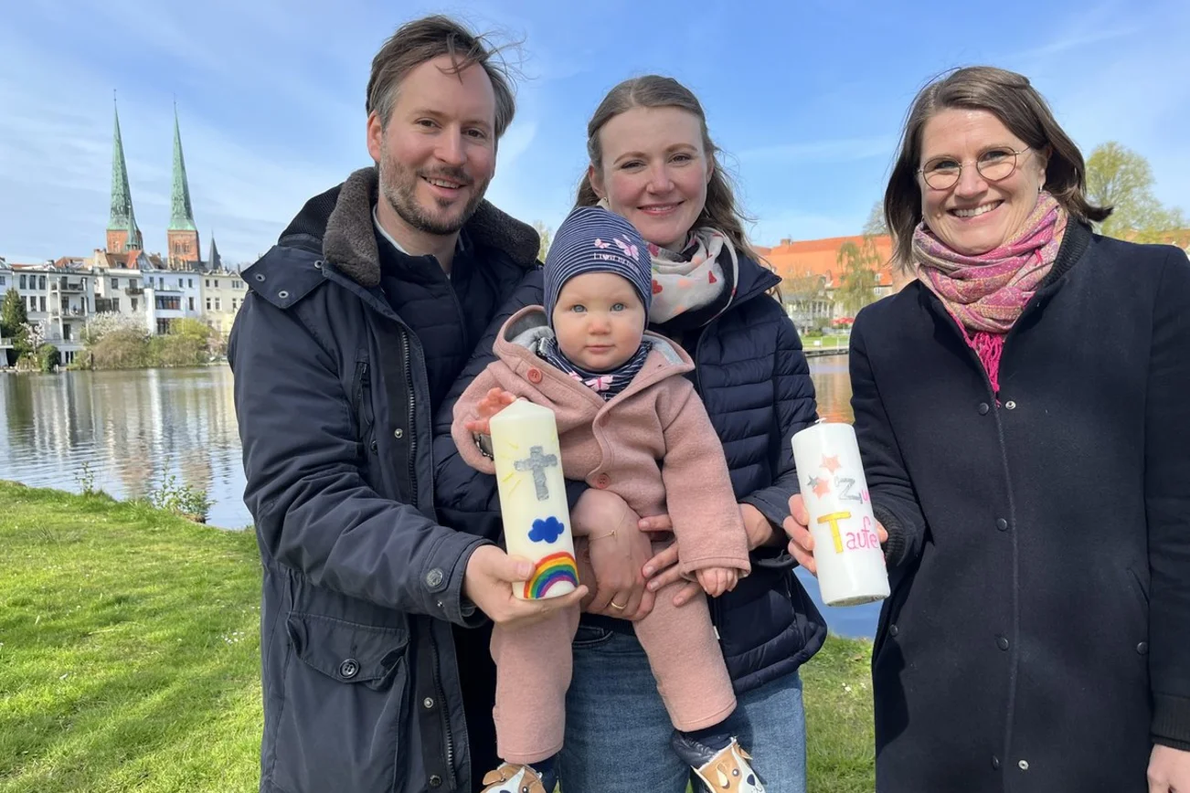 Eine Familie und eine Pastorin stehen vor einem Gewässer