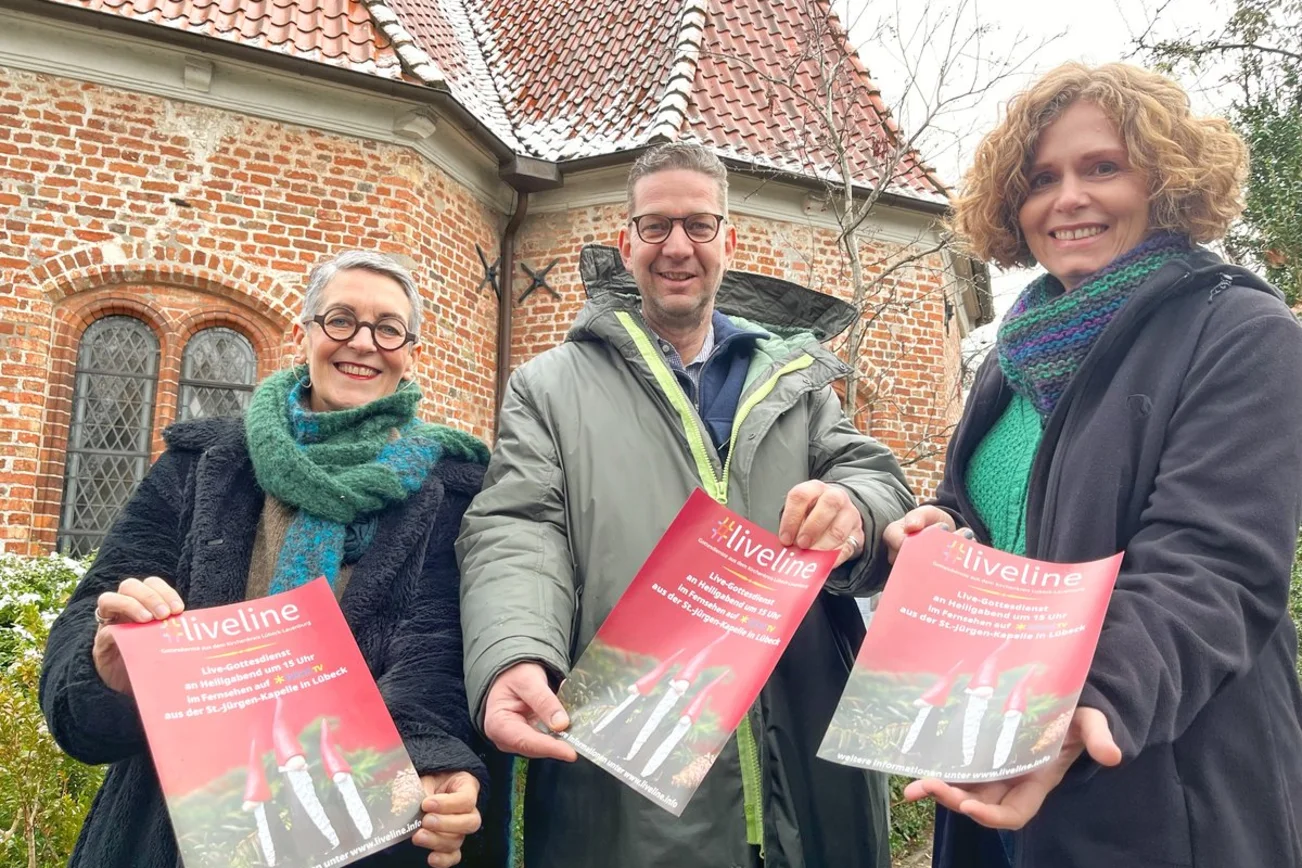Drei Menschen stehen mit einem Plakat vor einer Kapelle