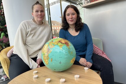 Zwei Frauen sitzen an einem Tisch, auf dem ein Globus Ball liegt. Darum stehen Teelichter. - Copyright: Annkathrin Bornholdt