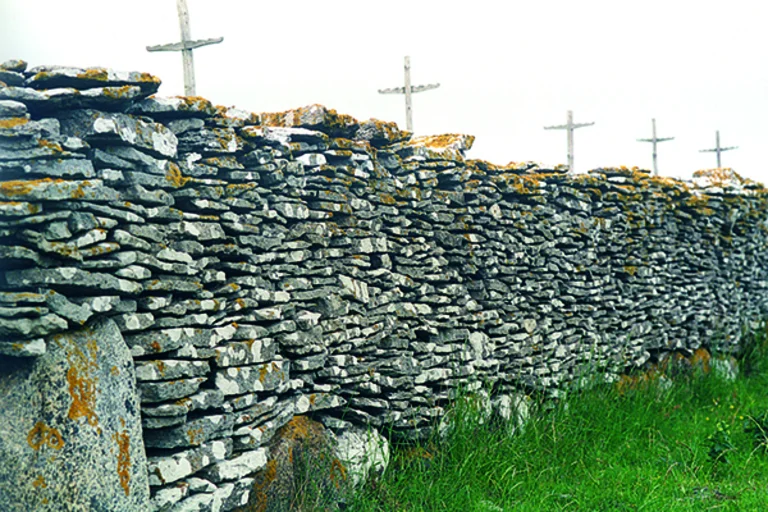 Holzkreuze hinter einer massiven Steinmauer aus vielen einzelnen flachen Steinen symbolisieren die Passion Christi