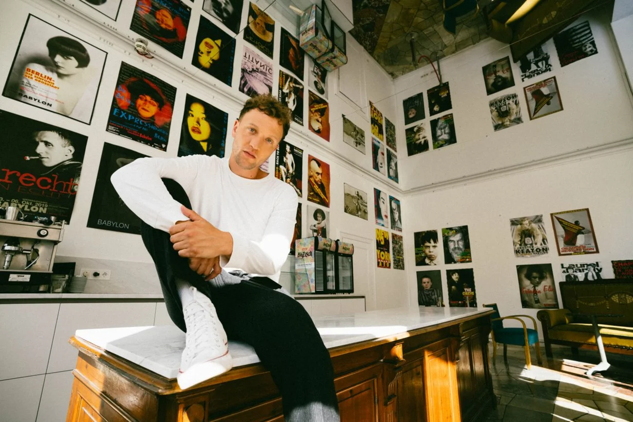 Ein junger Mann sitzt auf einem Tisch vor Wänden mit Plattencovern.