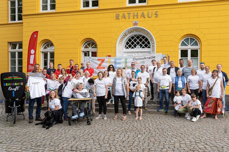 Eine großes Gruppenfoto von Menschen in weißen T-Shirts vor einem gelben Ratzhaus - Copyright: Jens Butz