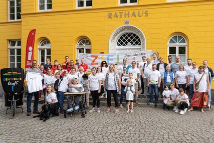Eine großes Gruppenfoto von Menschen in weißen T-Shirts vor einem gelben Ratzhaus - Copyright: Jens Butz