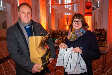 Zwei Personen stehen mit Geschenktüten in einer Kirche und lächeln in die Kamera.  - Copyright: Bastian Modrow