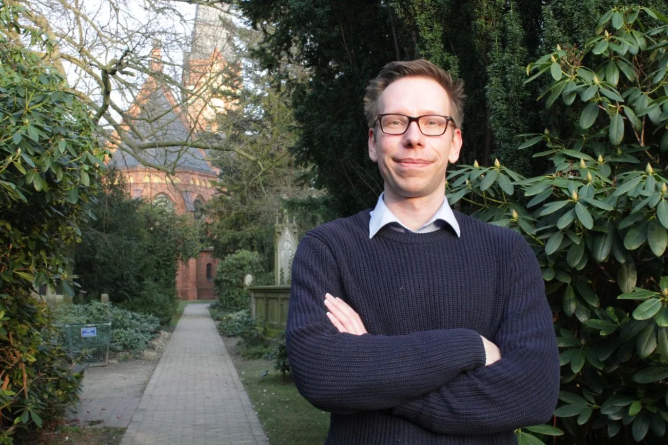 Junger Mann auf einem Friedhof vor einer Kirche.