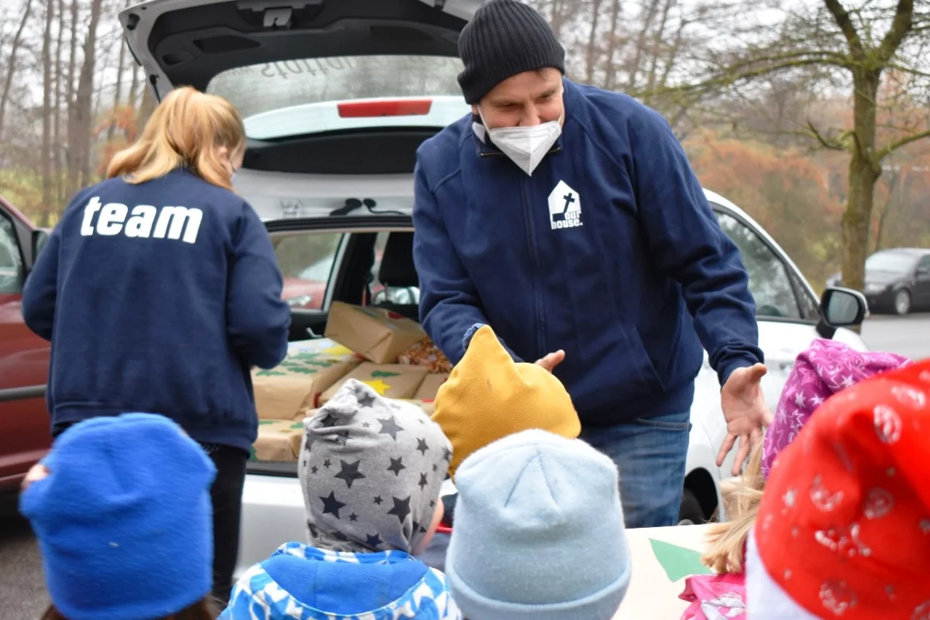 Kinder geben Pakete an Erwachsene. Sie laden diese in den Kofferraum eines Kleinwages.