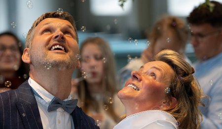 Ein Mann und eine Frau blicken lachend nach oben Seifenblasen hinterher.
