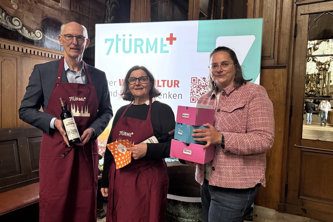 Ein Mann und zwei Frauen stehen vor einer 7Türme+ Werbewand.
