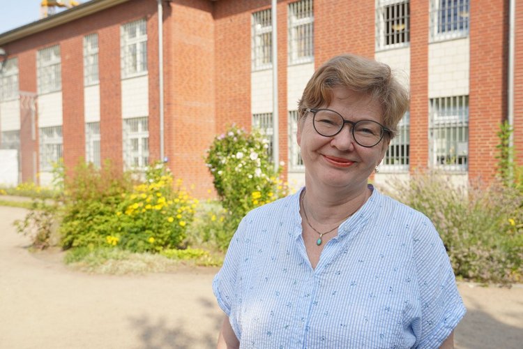 Eine Frau mit kurzen Haaren steht vor einer Hauswand mit Gitterfenstern. - Copyright: Annkathrin Bornholdt