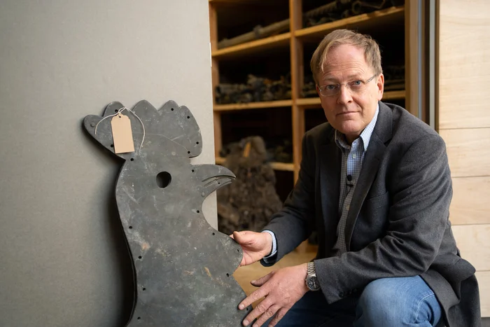 Ein Mann kniet neben einem Wetterhahn.