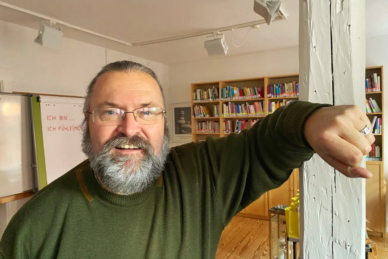 Ein Mann steht in einem Raum und lächelt in die Kamera.