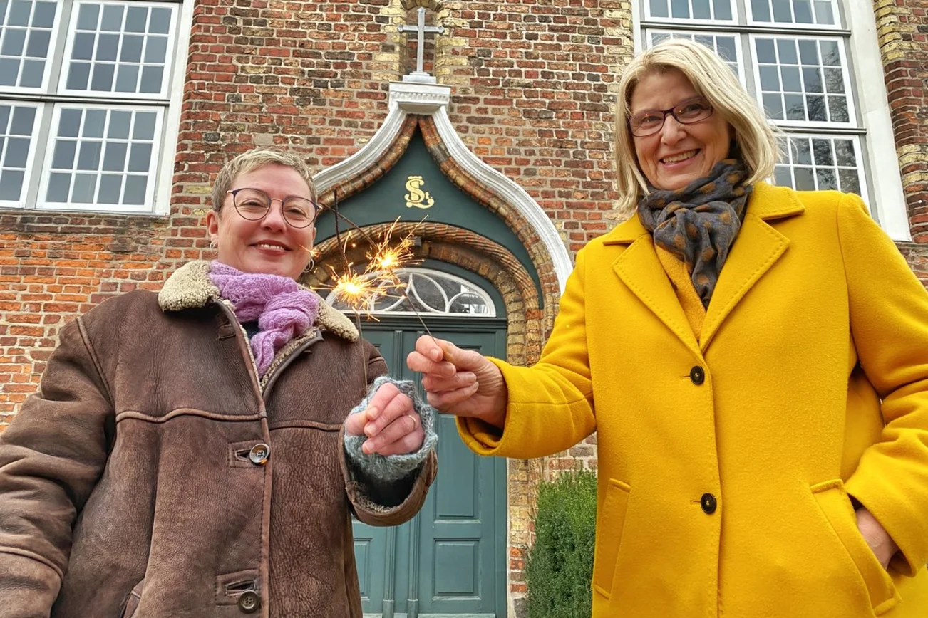 Zwei Personen stehen lächelnd mit Wunderkerzen vor einer Kirche.