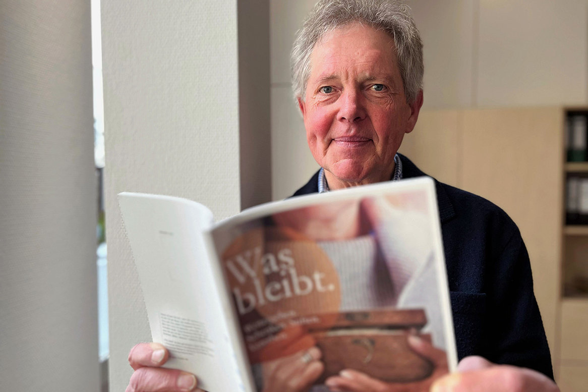 Fundraiser Wilfried Staake hält das Heft "Was bleibt."geöffnet in seinen Händen und schaut in die Kamera