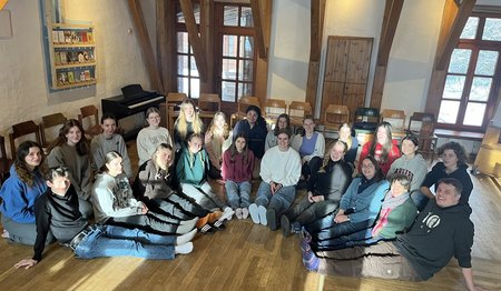 Eine Gruppe Schülerinnen und Schüler sitzt im Halbkreis in einem Raum mit Holzfußboden.