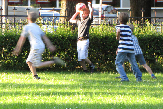 Vier Jungen spielen auf einem Rasen der Teils sonnenbeschienen ist. Der zweite Junge von links hält einen Ball über seinem Kopf - Copyright: Friedenskirche Lübeck