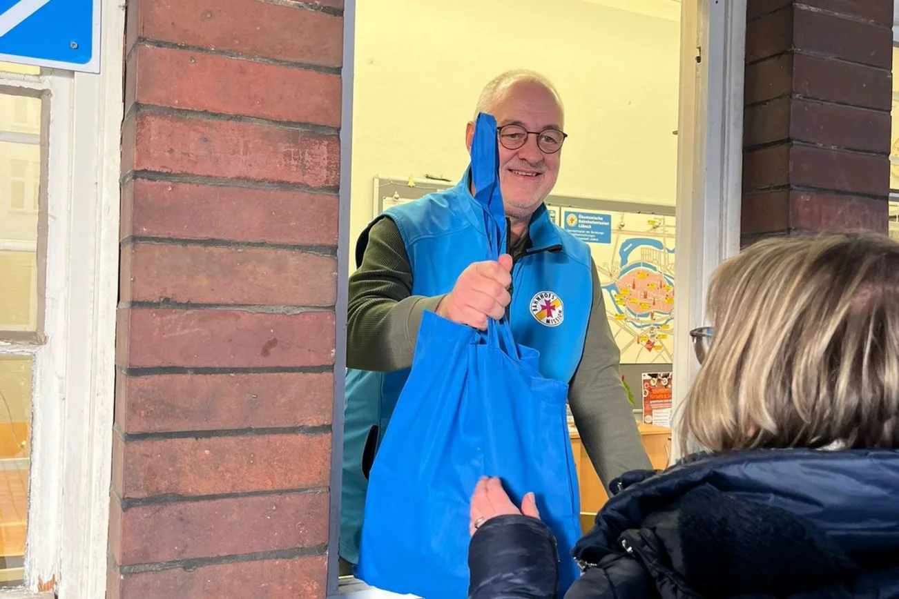 Ein Mann hält einen Beutel aus einem Fenster und eine Frau greift nach diesem Beutel.
