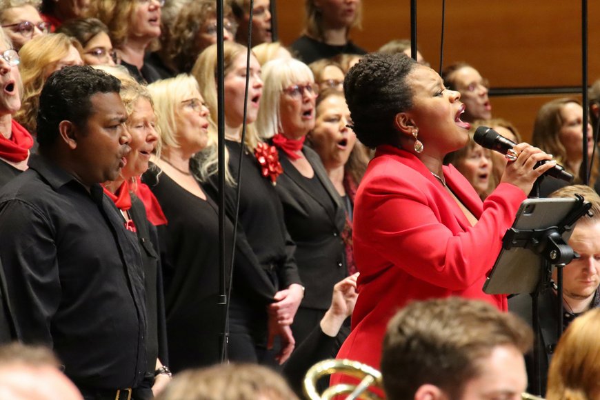 Eine schwarze Sängerin mit rotem Anzug steht inmitten eines Chores und singt.  - Copyright: Dirkt Tostmann