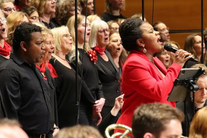 Eine schwarze Sängerin mit rotem Anzug steht inmitten eines Chores und singt.  - Copyright: Dirkt Tostmann