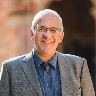 Ein Mann mit kurzen grauen Haaren, Brille und einem grauen Sakko lächelt in die Kamera