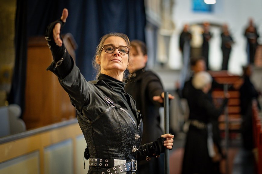 Eine Frau in schwarzer Kleidung steht in einer Kirche und macht eine ausladende theatralische Geste. - Copyright: Jens Butz