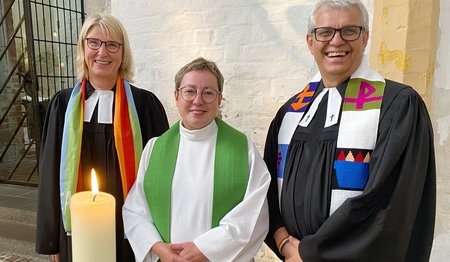 Zwei Frauen und ein Mann stehen in einer Kirche.