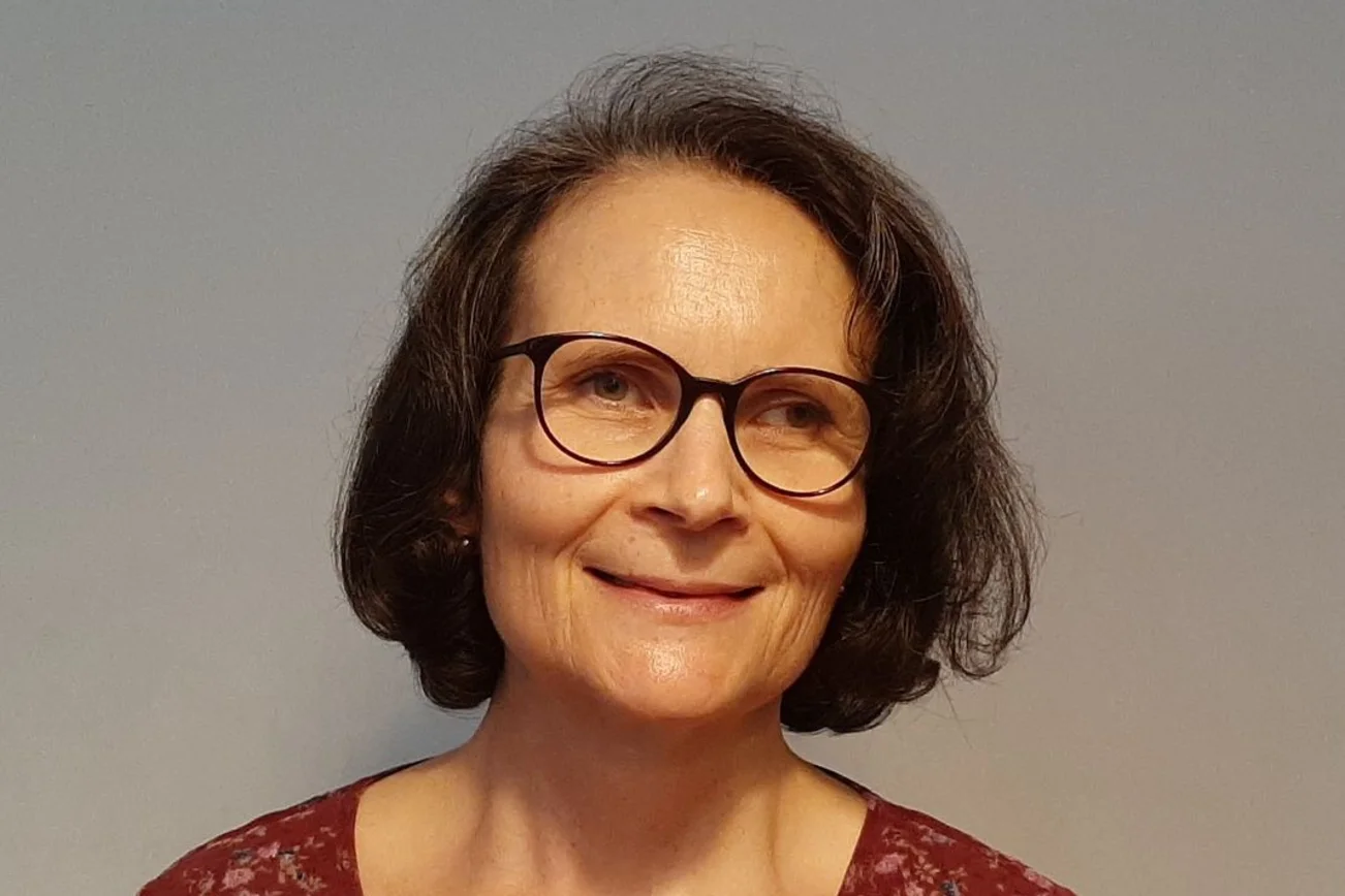 Eine Frau mit dunklen halblangen Haaren und einer dunklen Brille lächelt freundlich in die Kamera.