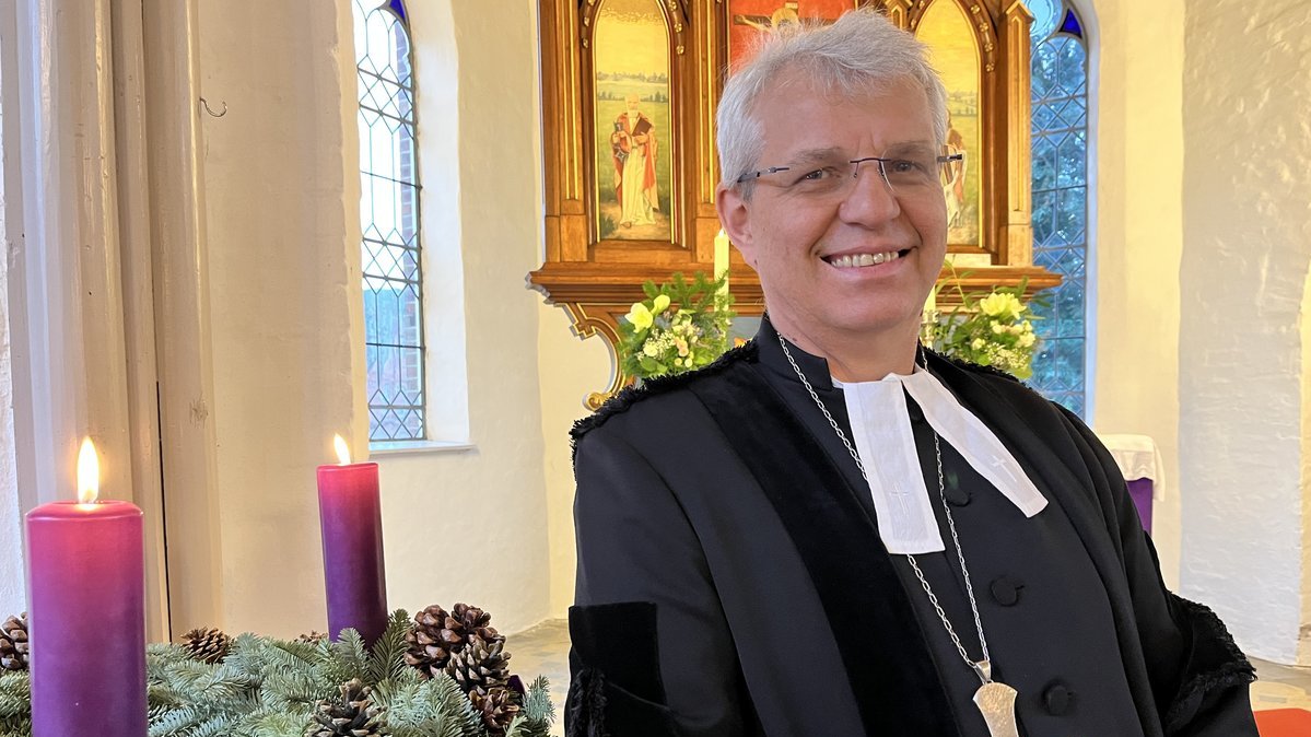 Ein Mann steht in einer Kirche an einem Adventskranz