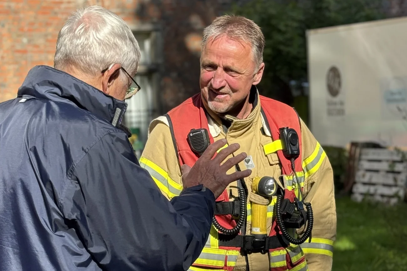 Ein Mann mit in Feuerwehr-Uniform spricht mit einem Mann in einer blauen Jacke.
