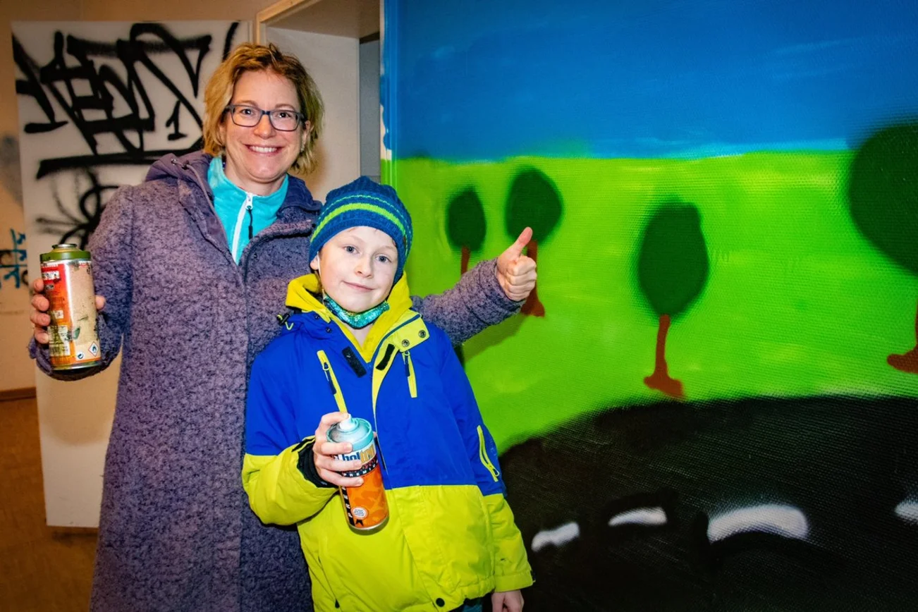 Eine Mutter und ihr Sohn stehen vor einer gesprayten Wand.