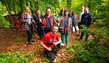 Eine Gruppe junger Menschen steht vor dem Auflieger eines Anhängers im Wald. 