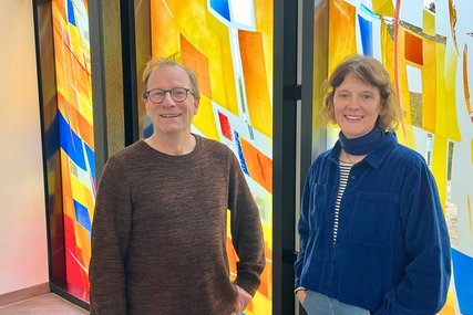 Ein Mann und eine Frau stehen nebeneinander vor den bunten Fenstern des 'Raums der Stille'. - Copyright: Katharina Micheel