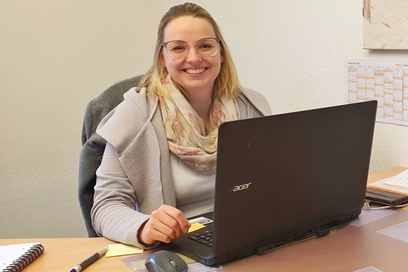 Frau sitzt lächelnd an ihrem Laptop.